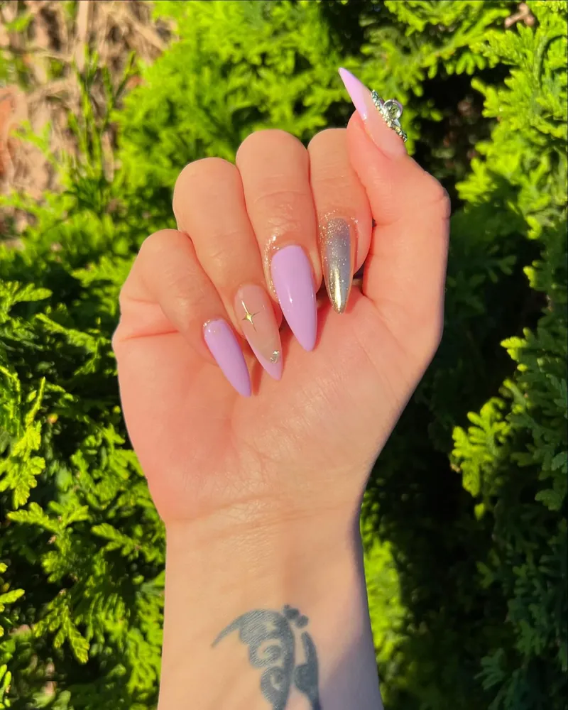 Lilac almond nails with a chrome accent nail, held up against garden greenery